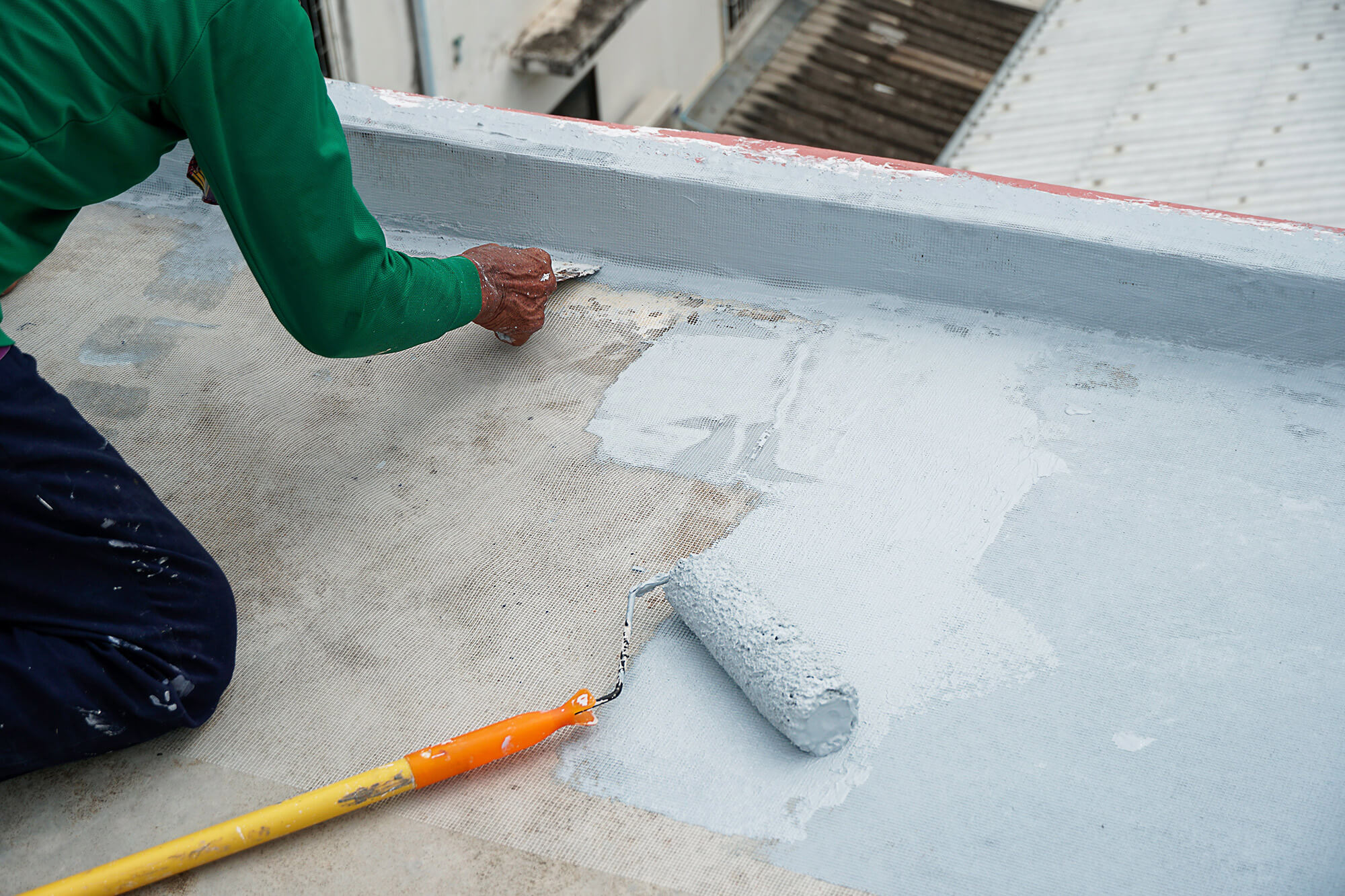 Worker applying polyurethane waterproof membrane on flat terrace roof
